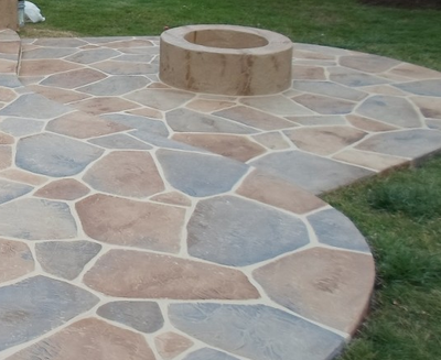 Multiple shades of brown and gray stained decorative patio with a built in round fire pit.